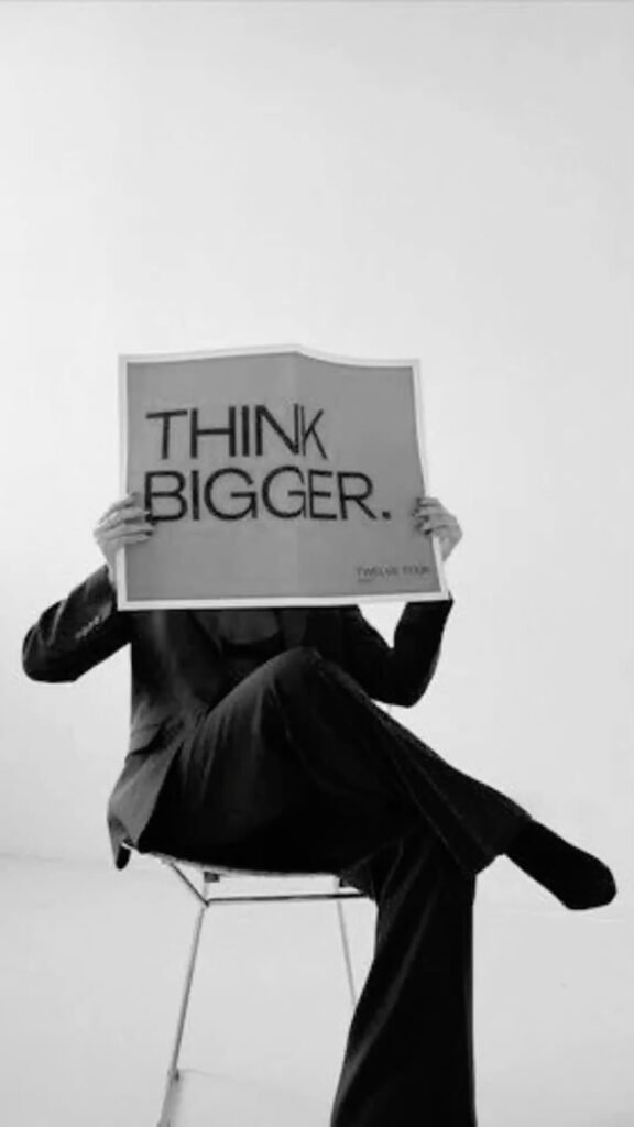 A person in a business suit holding a "Think Bigger" sign, representing growth mindset, strategic thinking, innovation, and business success.